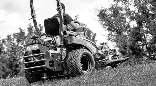 A person uses a Ferris® zero-turn mower to cut grass.