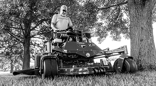 A person uses a Ferris® stand-on mower to cut grass.