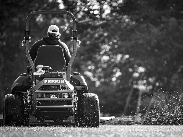A person uses a Ferris® riding lawn mower to cut grass.